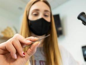 Biology student Olivia Nunn holds an ant in tweezers next to a microscope.